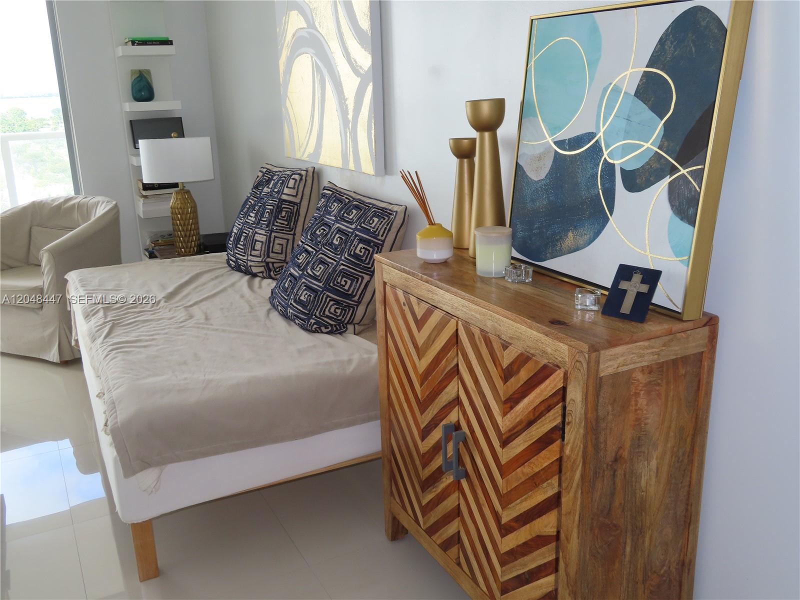A bedroom features a daybed, a chevron-patterned wooden cabinet, and abstract wall art — 5701 Collins Ave # 1703, Miami Beach FL 33140, MIAMI BEACH, FL