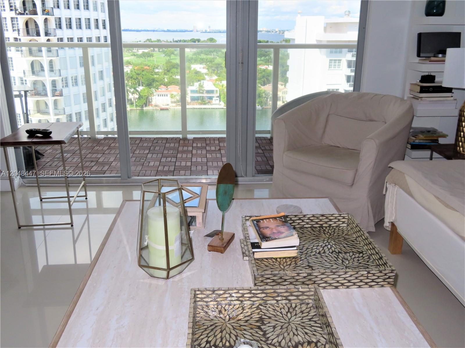 A living room features a marble coffee table, a beige armchair, and a balcony view — 5701 Collins Ave # 1703, Miami Beach FL 33140, MIAMI BEACH, FL
