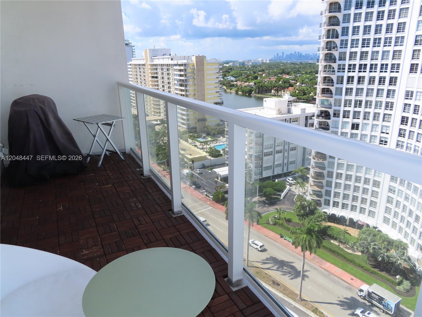 A balcony with wood-look flooring overlooks a street, a canal, and nearby high-rise buildings — 5701 Collins Ave # 1703, Miami Beach FL 33140, MIAMI BEACH, FL
