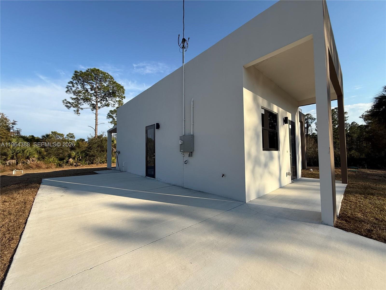 A white, modern-style building features a concrete patio and a covered entrance area — 133 Nacelle ave, Lehigh Acres FL 33974, LEHIGH ACRES, FL