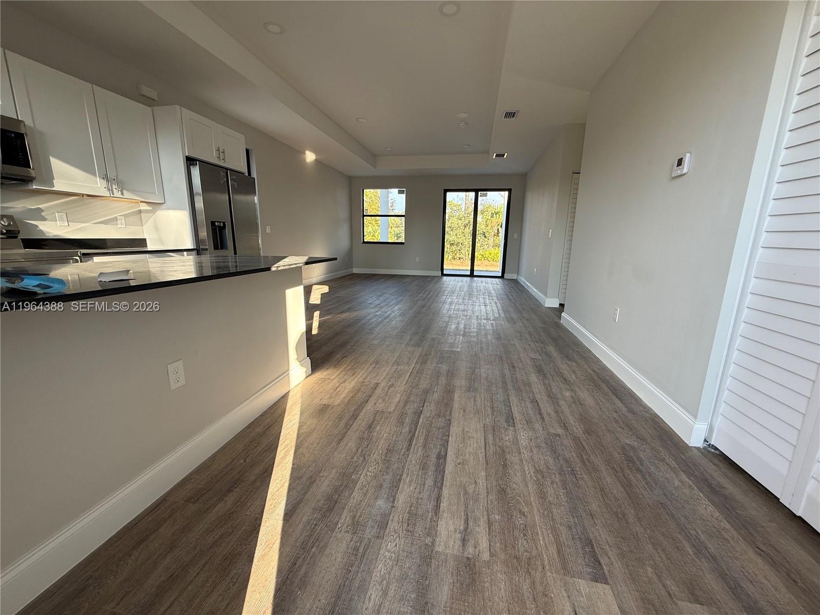 An open-concept kitchen and living area features wood-look flooring, white cabinets, and sliding glass doors — 133 Nacelle ave, Lehigh Acres FL 33974, LEHIGH ACRES, FL