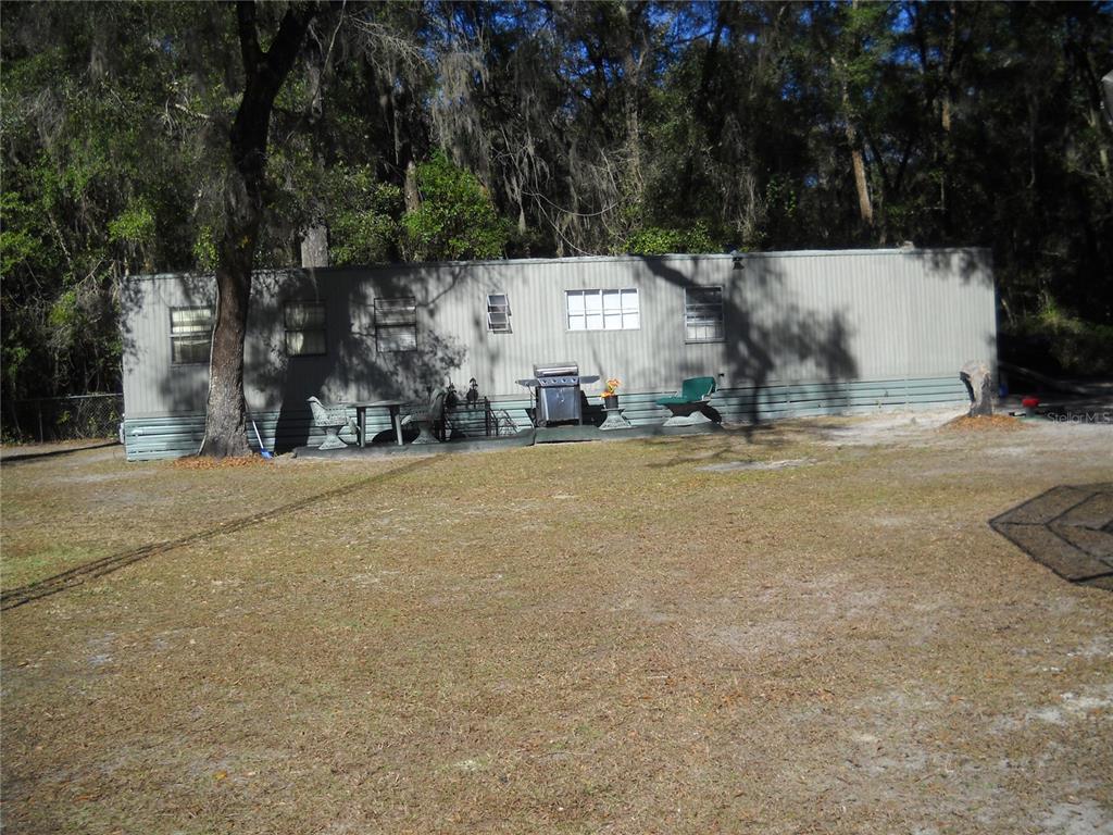 A single-story mobile home sits on a grassy lot surrounded by trees — 4881 NW 69TH STREET, OCALA, FL