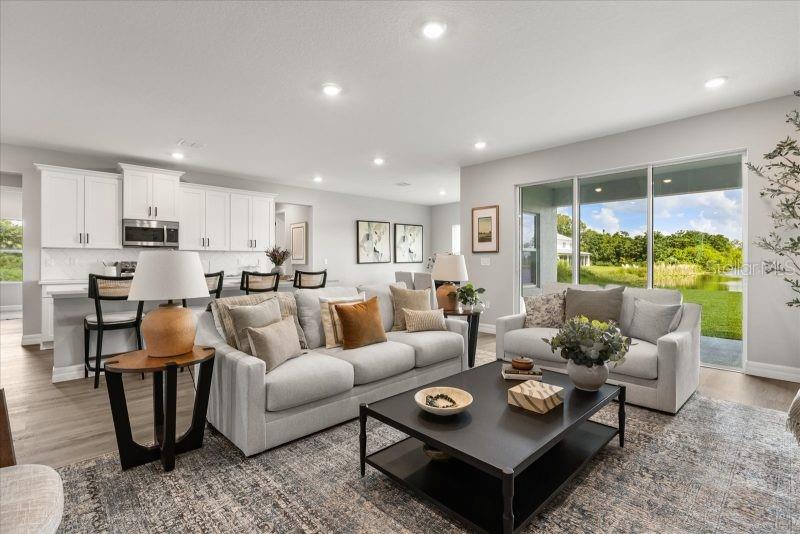 A living room with light gray walls, a sectional sofa, and a kitchen in the background — 13381 SW 75TH COURT, OCALA, FL