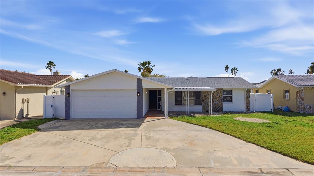 A single-story house features a white garage, stone accent wall, and a concrete driveway — 3928 RUDDER WAY, NEW PORT RICHEY, FL