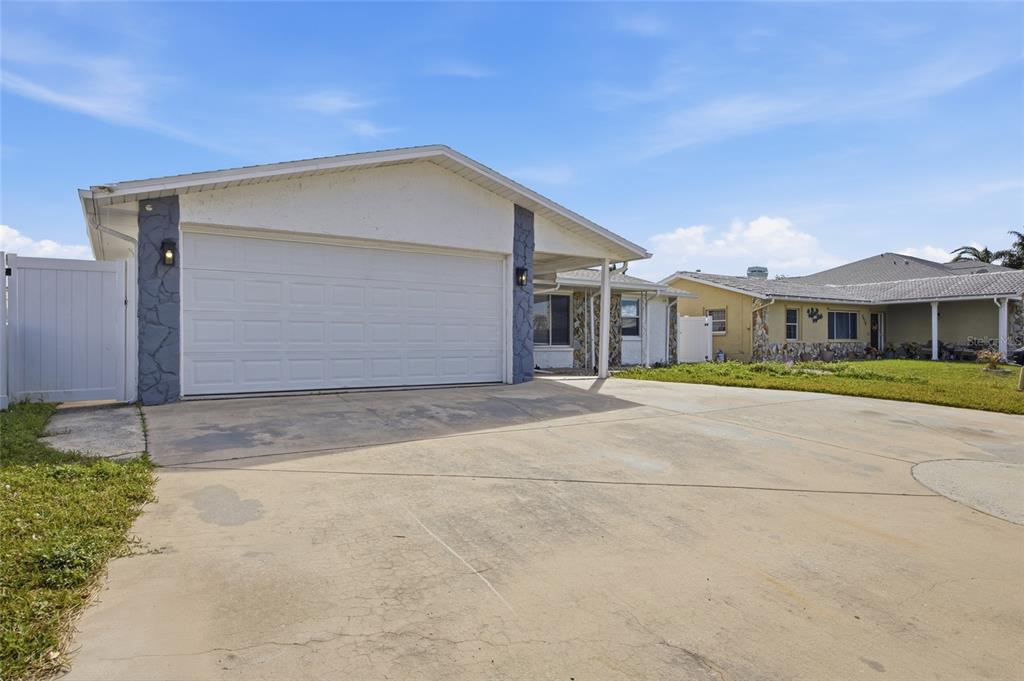 A single-story house features a white garage door, stone-accented pillars, and a concrete driveway — 3928 RUDDER WAY, NEW PORT RICHEY, FL