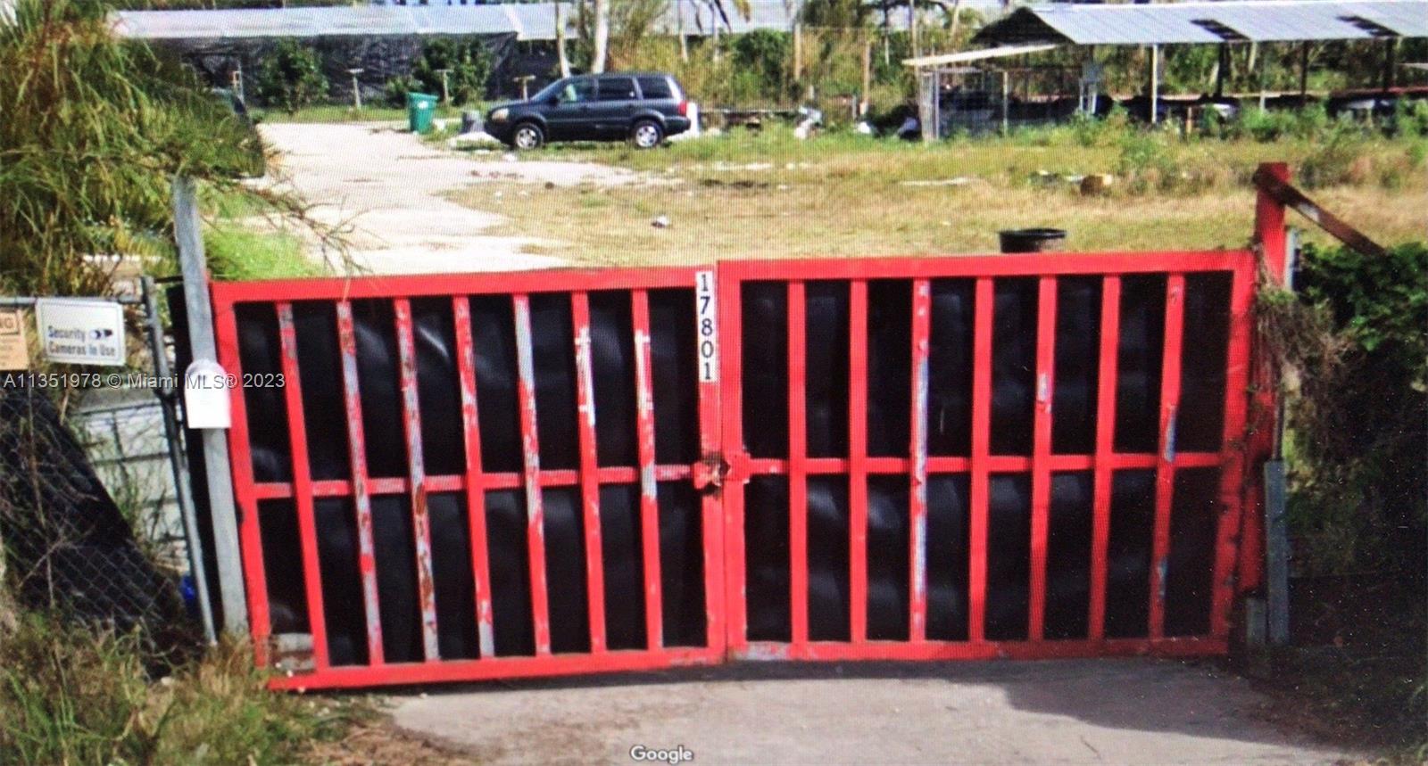 A red metal gate stands at the entrance of a gravel driveway with a parked vehicle — 17801 SW 197 Ave, Miami FL 33187, MIAMI, FL