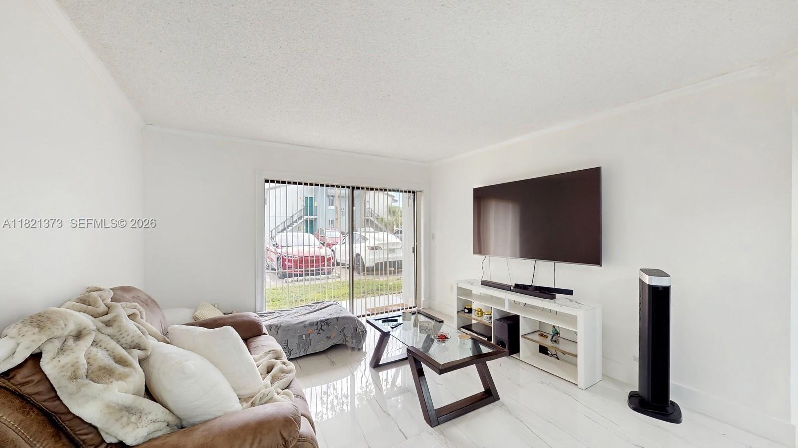 A living room features a brown sofa, a glass coffee table, and a wall-mounted television — 7180 NW 179th St # 105, Hialeah FL 33015, HIALEAH, FL