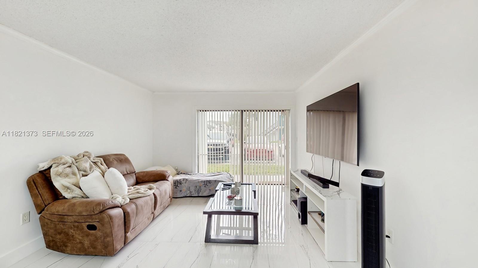 A living room features a brown sofa, a glass coffee table, and a wall-mounted television — 7180 NW 179th St # 105, Hialeah FL 33015, HIALEAH, FL