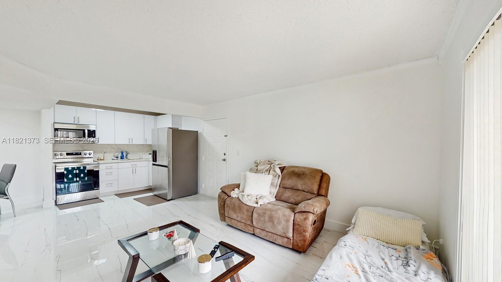 A living room with white tile floors, a brown loveseat, and an adjacent kitchen area — 7180 NW 179th St # 105, Hialeah FL 33015, HIALEAH, FL