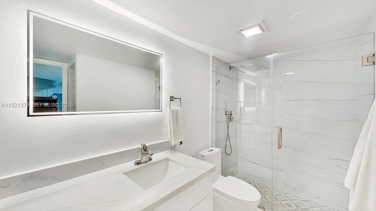 A modern bathroom features a white vanity, a backlit mirror, and a glass-enclosed marble shower — 7180 NW 179th St # 105, Hialeah FL 33015, HIALEAH, FL