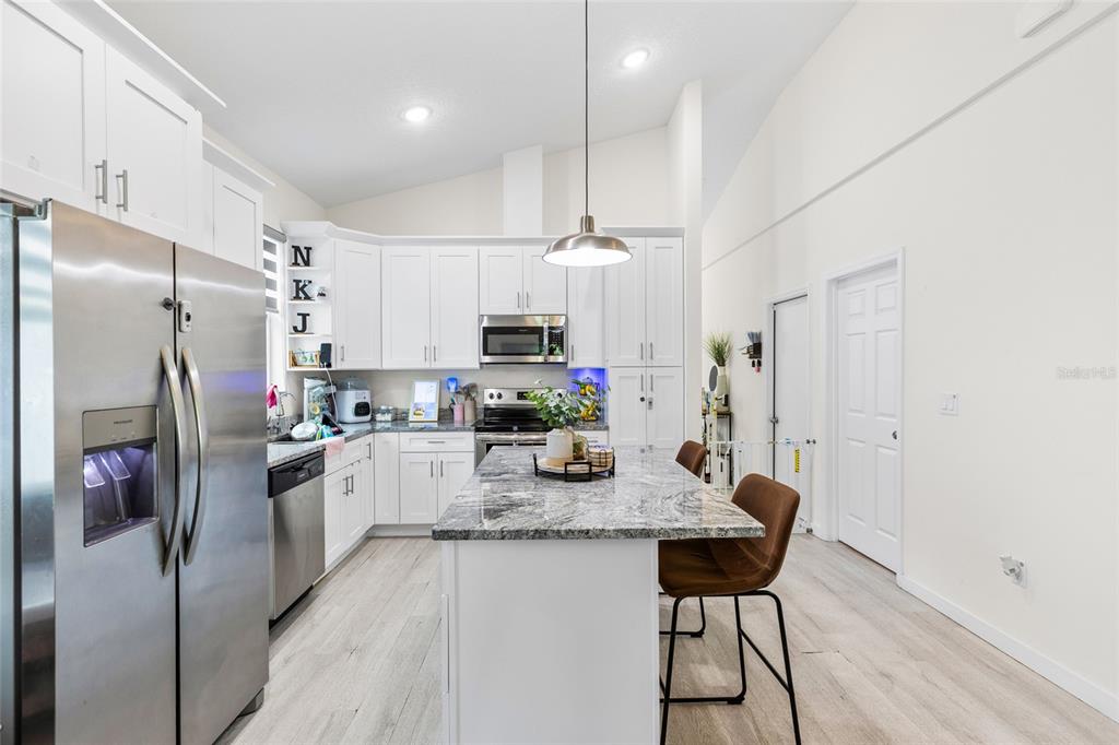 A modern kitchen features white cabinetry, granite countertops, a central island, and stainless steel appliances — 1747 S OAK STREET, SEFFNER, FL
