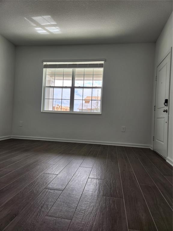 An empty room features dark wood-look flooring, white walls, a window, and a door — 997 WATERFALL BOULEVARD, DAVENPORT, FL