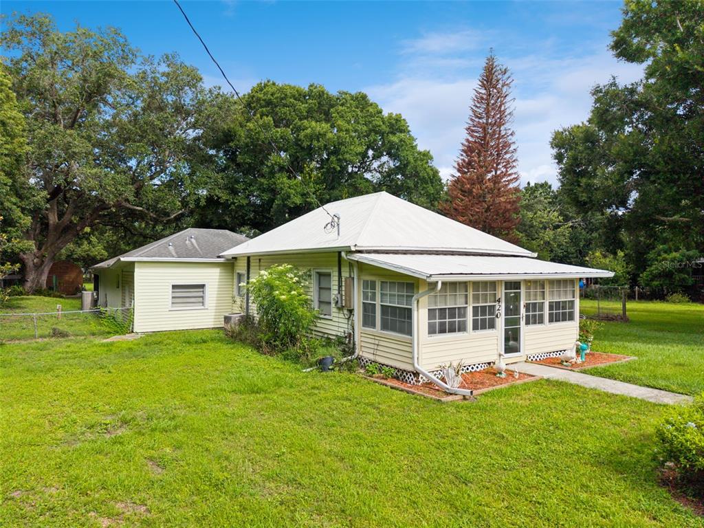 A yellow, single-story house with a metal roof and a screened-in front porch — 420 JACKS MEMORIAL RD, ST CLOUD, FL