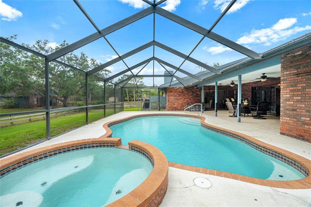 A screened-in patio features a brick-trimmed swimming pool and a raised circular hot tub — 140 COWPEN LANE, SARASOTA, FL