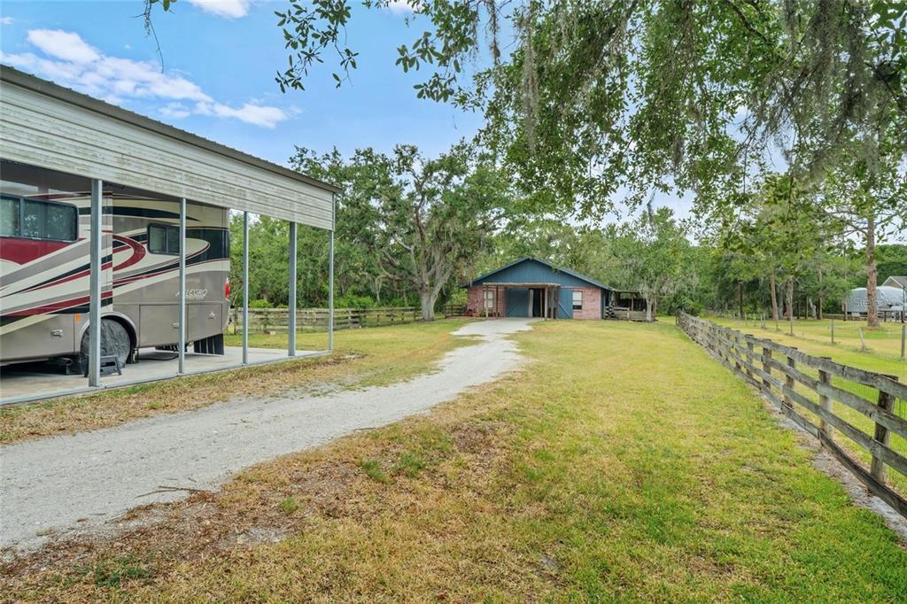 A gravel driveway leads to a blue house with a covered porch and RV shelter — 140 COWPEN LANE, SARASOTA, FL