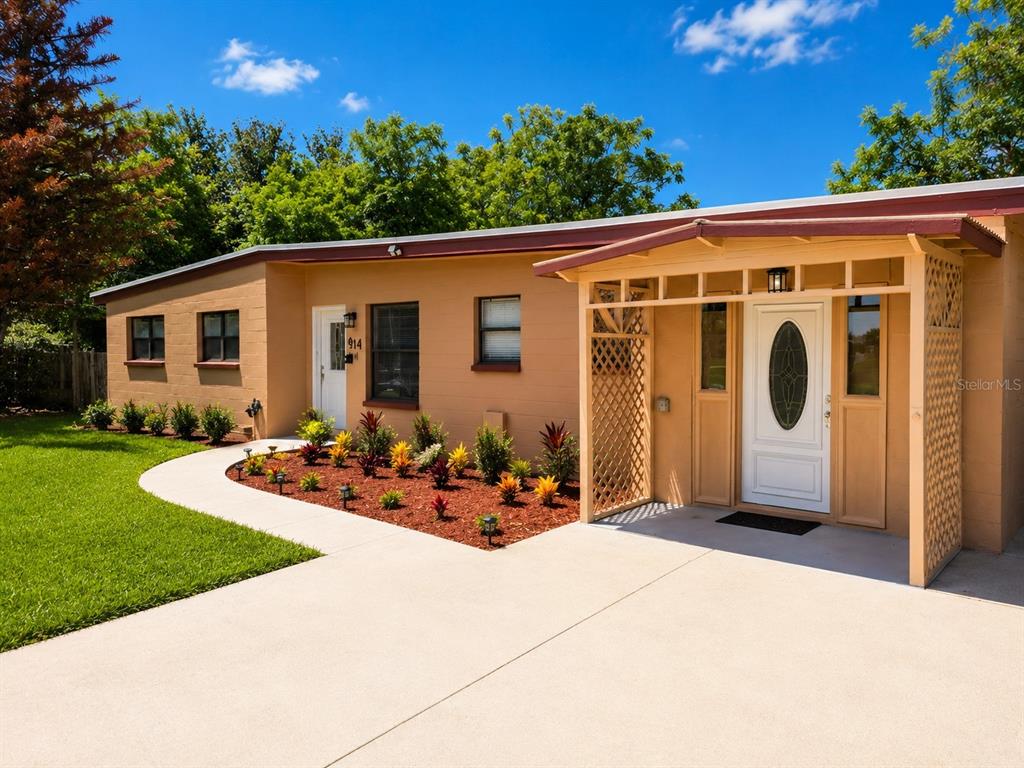 A tan, single-story house features a front porch, a concrete walkway, and a landscaped garden — 14 JAPONICA DRIVE, ORLANDO, FL