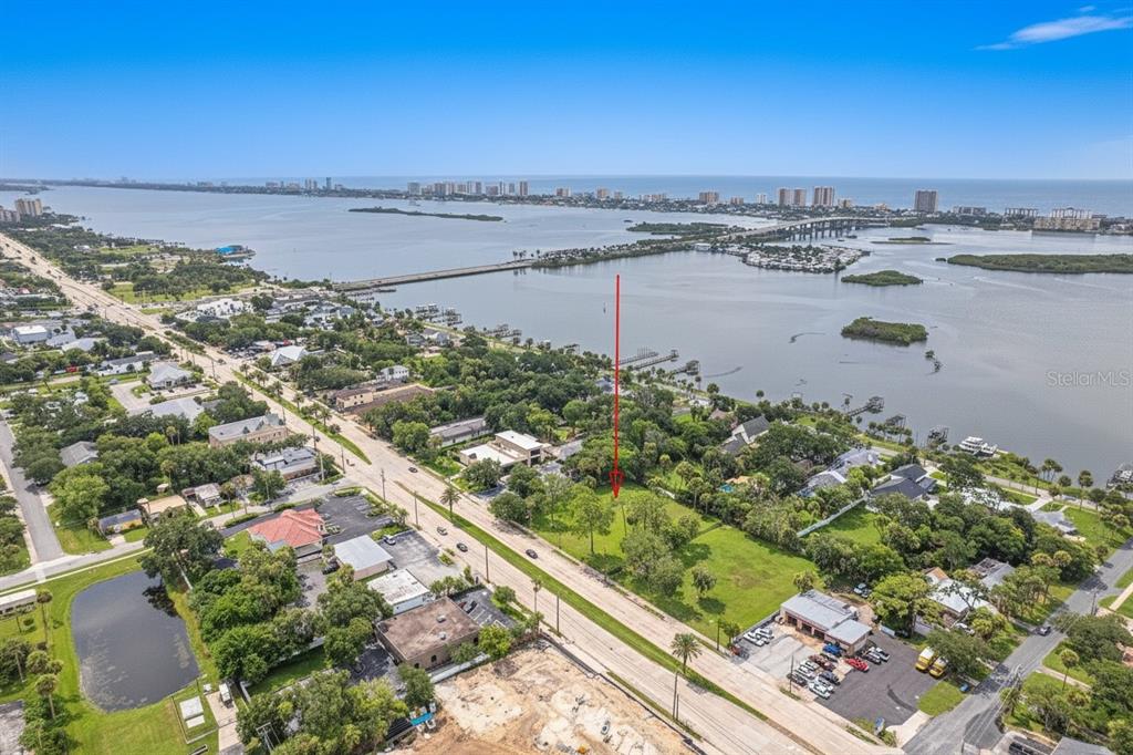 An aerial view shows a vacant, tree-lined lot situated along a road near the water — 4491 S RIDGEWOOD AVENUE, PORT ORANGE, FL