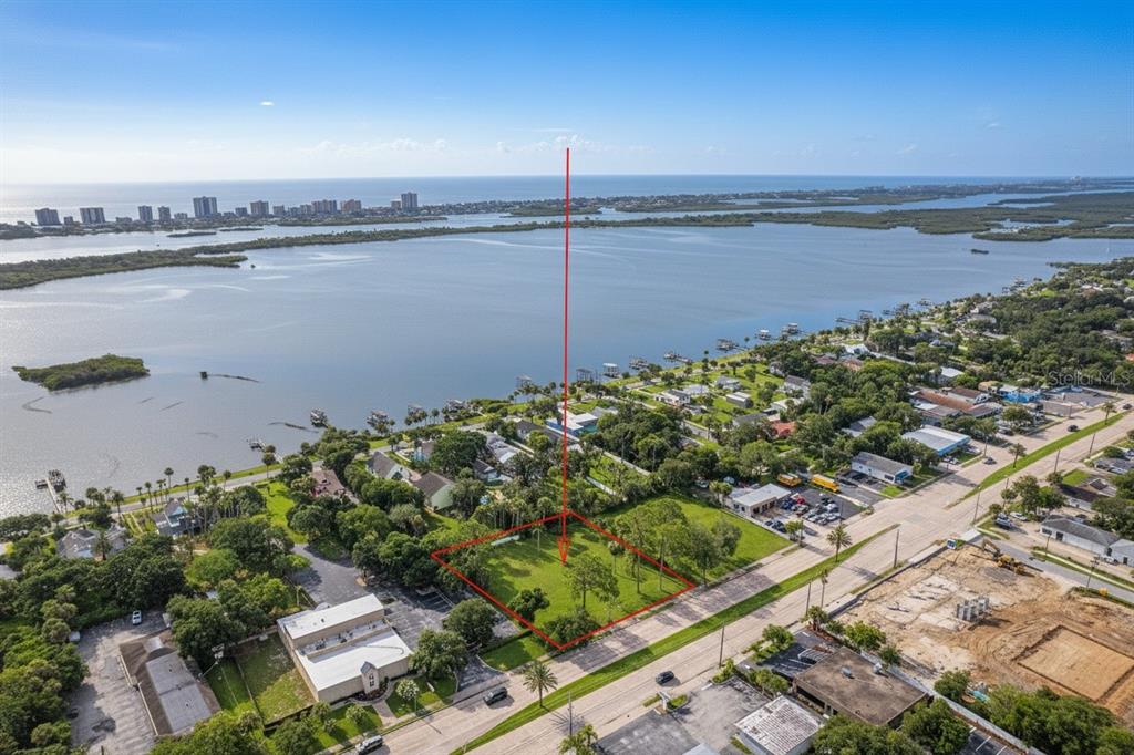 An aerial view shows a vacant, rectangular grassy lot outlined in red near a bay — 4491 S RIDGEWOOD AVENUE, PORT ORANGE, FL