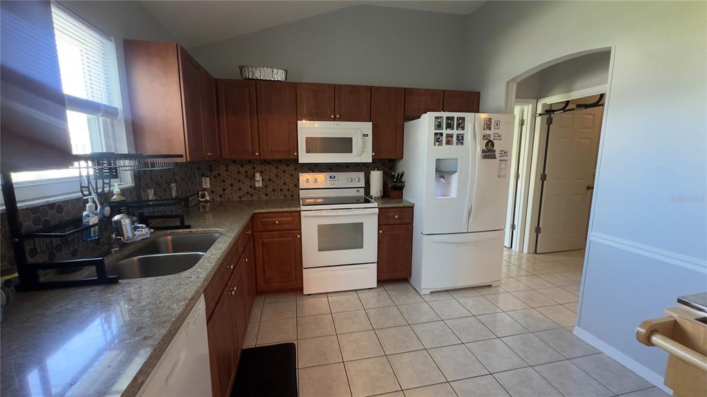 A kitchen features wood cabinets, granite countertops, white appliances, and a tiled floor — 2259 MARGARITA DRIVE, THE VILLAGES, FL