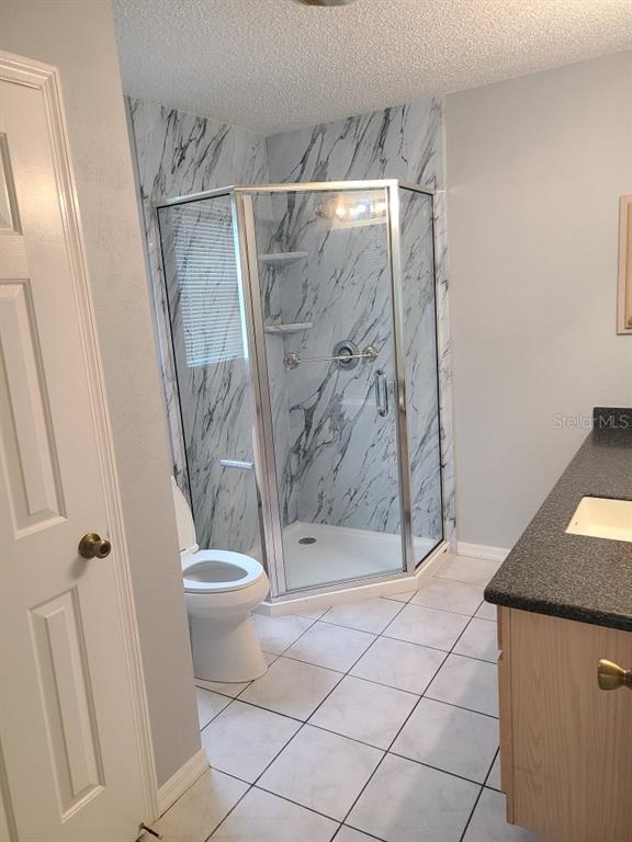 A bathroom features a corner glass shower with marble-patterned walls, a toilet, and tiled flooring — 2259 MARGARITA DRIVE, THE VILLAGES, FL