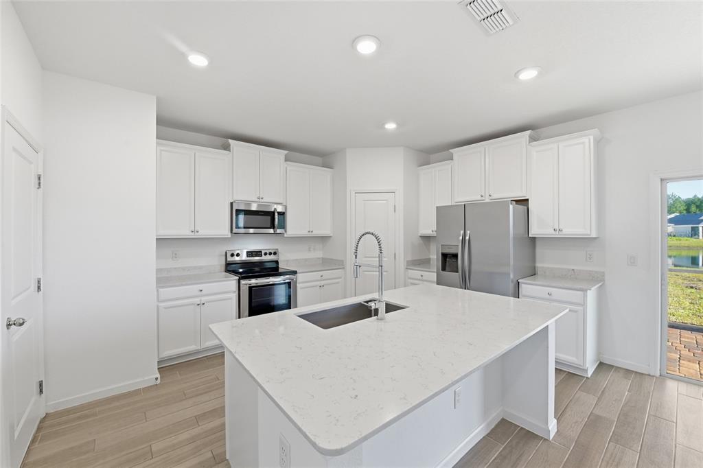 A modern kitchen features white cabinets, stainless steel appliances, and a central quartz island — 9852 LEMON BALM WAY, JACKSONVILLE, FL
