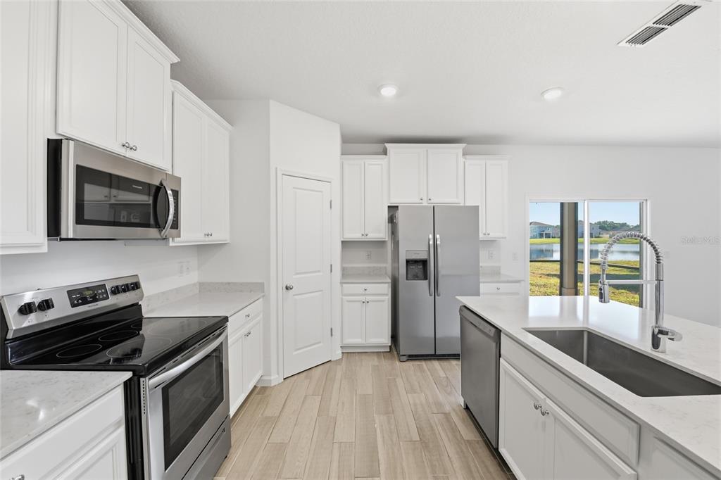 A modern kitchen features white cabinets, stainless steel appliances, quartz countertops, and a water view — 9852 LEMON BALM WAY, JACKSONVILLE, FL