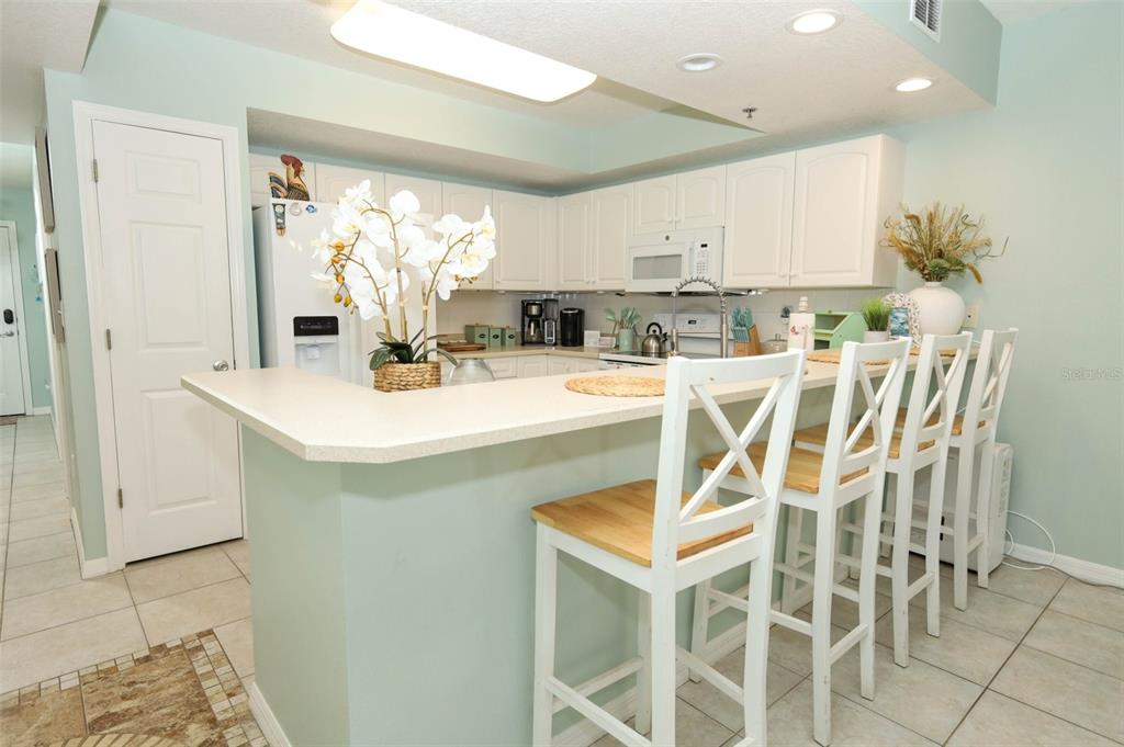 A kitchen features white cabinetry, a breakfast bar with four stools, and light-colored walls — 5300 S ATLANTIC AVE UNIT 9-304, NEW SMYRNA BEACH, FL