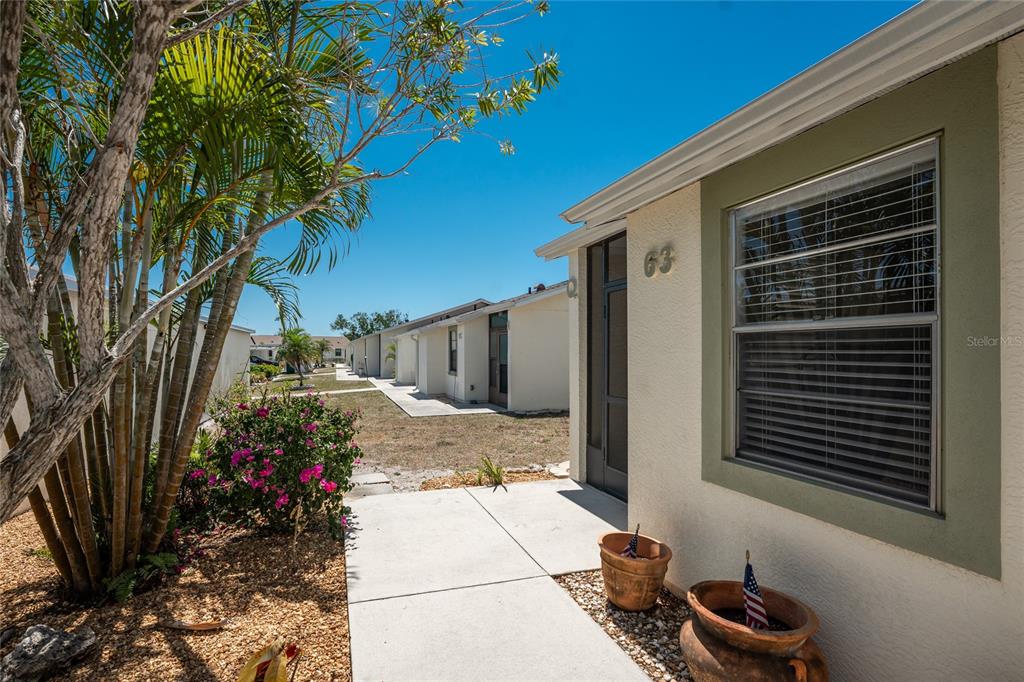 A view of a building exterior with a concrete walkway, potted plants, and landscaping — 6796 GASPARILLA PINES BOULEVARD UNIT 63, ENGLEWOOD, FL