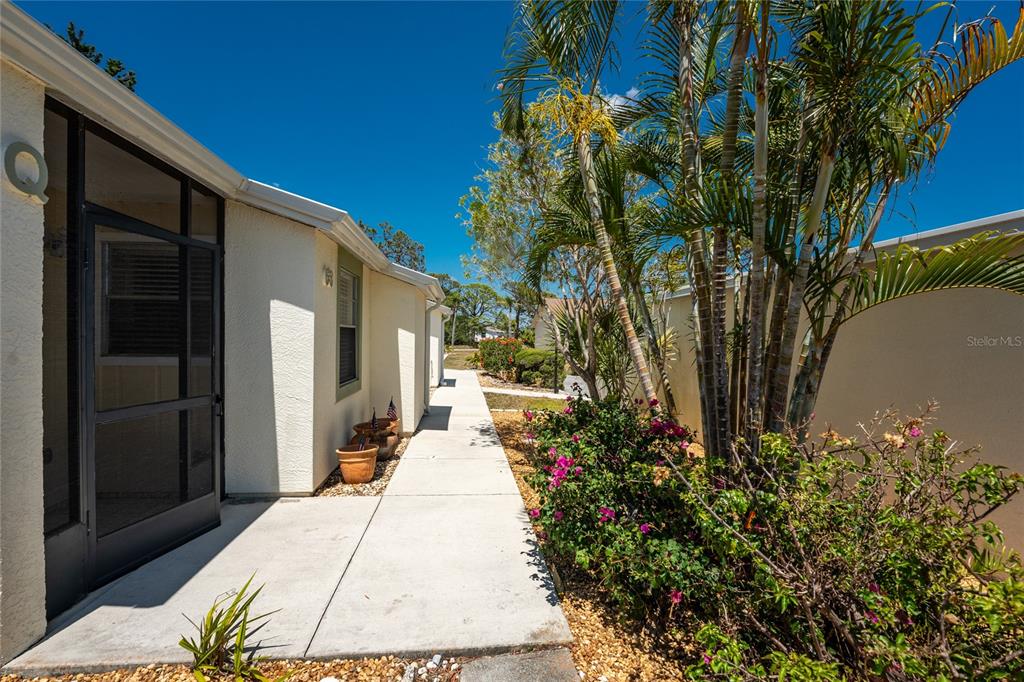 A paved walkway leads past a house exterior with a screened door and palm trees — 6796 GASPARILLA PINES BOULEVARD UNIT 63, ENGLEWOOD, FL