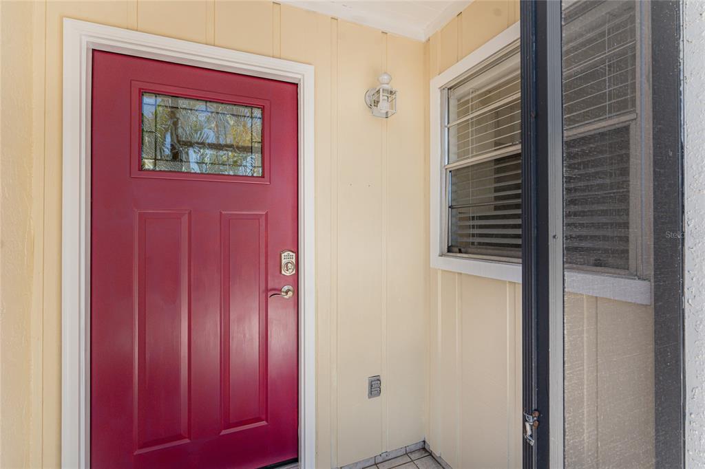 A red front door with a window sits next to a window on a porch — 6796 GASPARILLA PINES BOULEVARD UNIT 63, ENGLEWOOD, FL