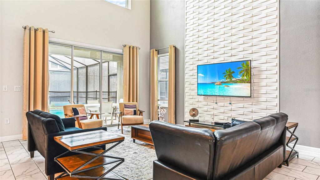 A living room features a textured white accent wall, a television, and sliding glass doors — 2791 PUNCTUATION PLACE, KISSIMMEE, FL