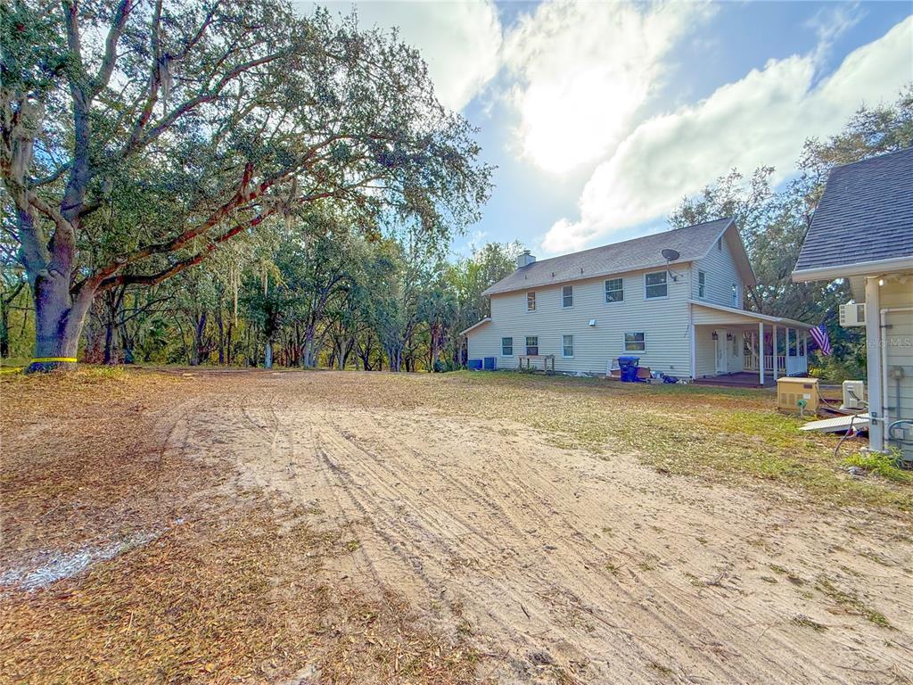 A two-story house with light siding sits on a large, sandy lot with mature trees — 2827 SANCTUARY LANE, WINTER GARDEN, FL