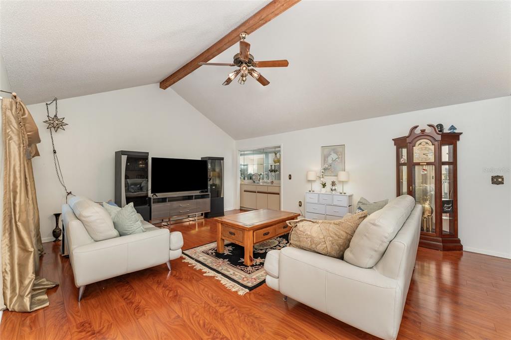 A living room features a vaulted ceiling with a wood beam, hardwood floors, and two sofas — 4240 CREEKWOOD LANE, MULBERRY, FL