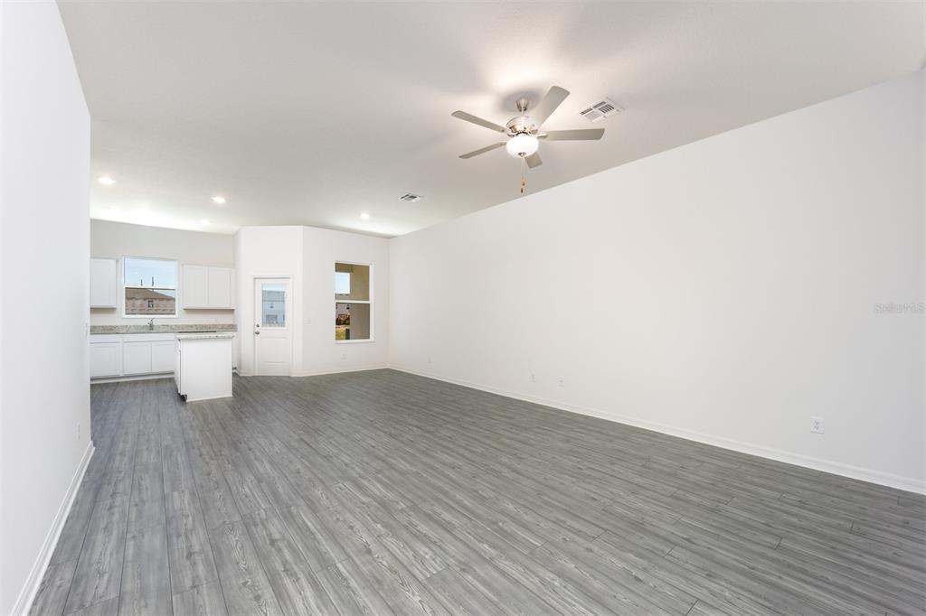 An open-concept living area features gray wood-look flooring, white walls, and an adjacent kitchen — 709 POPPY LANE, DUNDEE, FL