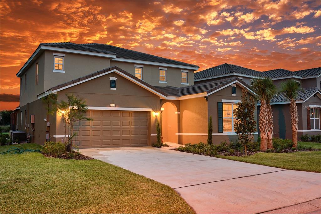 A two-story suburban house with a tan stucco exterior, a garage, and a concrete driveway — 5231 WILDWOOD WAY, DAVENPORT, FL