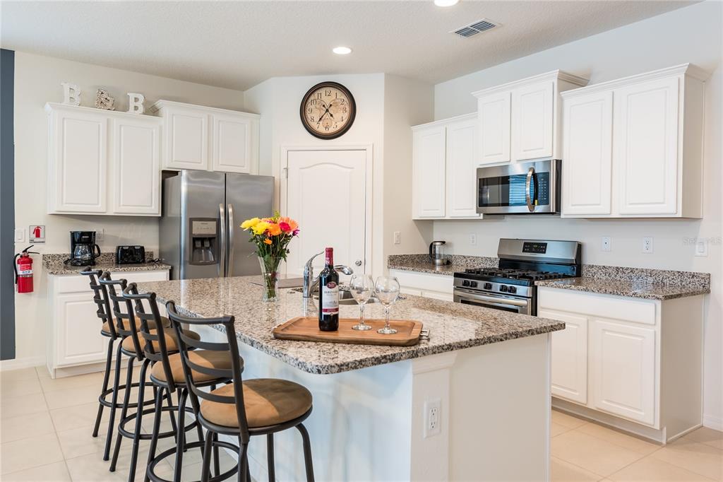 A kitchen features white cabinets, granite countertops, a center island with stools, and stainless appliances — 5231 WILDWOOD WAY, DAVENPORT, FL