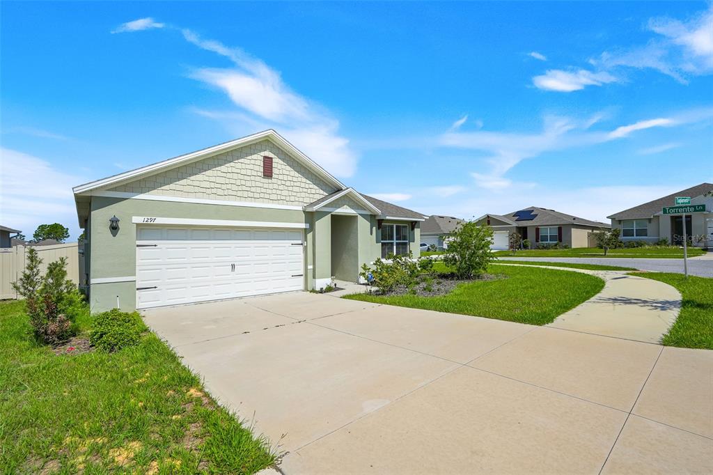 A single-story house with a light green exterior, a two-car garage, and a concrete driveway — 1297 TAGLIAMENTO LANE, HAINES CITY, FL