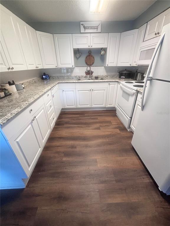 A kitchen features white cabinets, granite countertops, stainless steel appliances, and dark wood-look flooring — 4824 8TH STREET, ZEPHYRHILLS, FL
