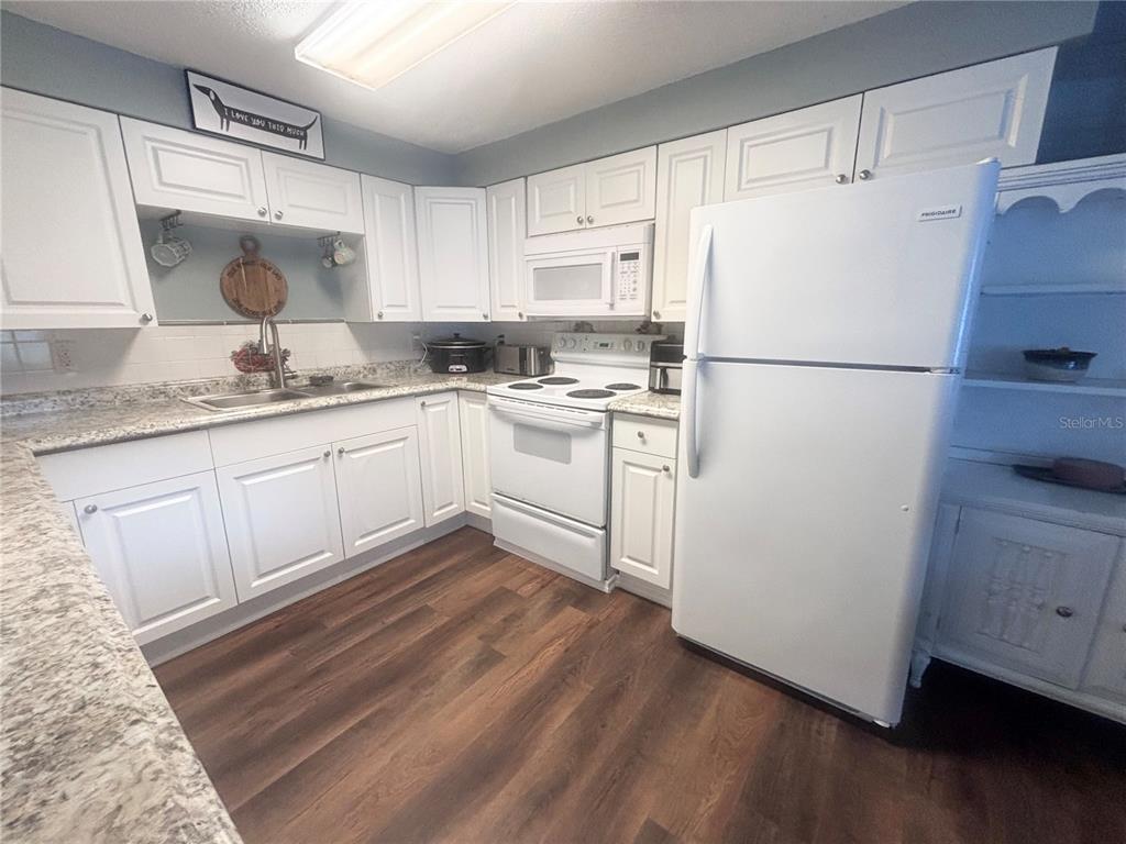 A kitchen features white cabinets, granite countertops, white appliances, and wood-look flooring — 4824 8TH STREET, ZEPHYRHILLS, FL