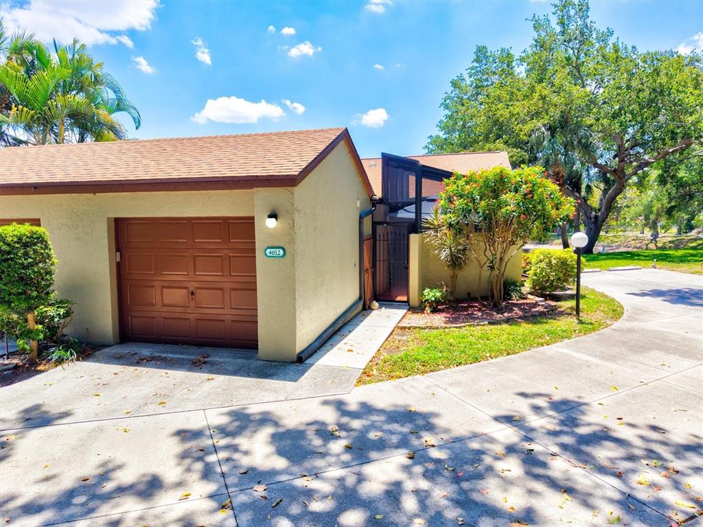A tan house with a brown garage door and a screened entryway under a blue sky — 4612 PARK LAKE TERRACE N, BRADENTON, FL