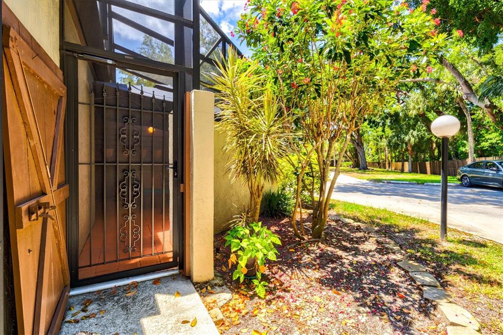 A metal security door leads to a screened entryway next to a tree and driveway — 4612 PARK LAKE TERRACE N, BRADENTON, FL