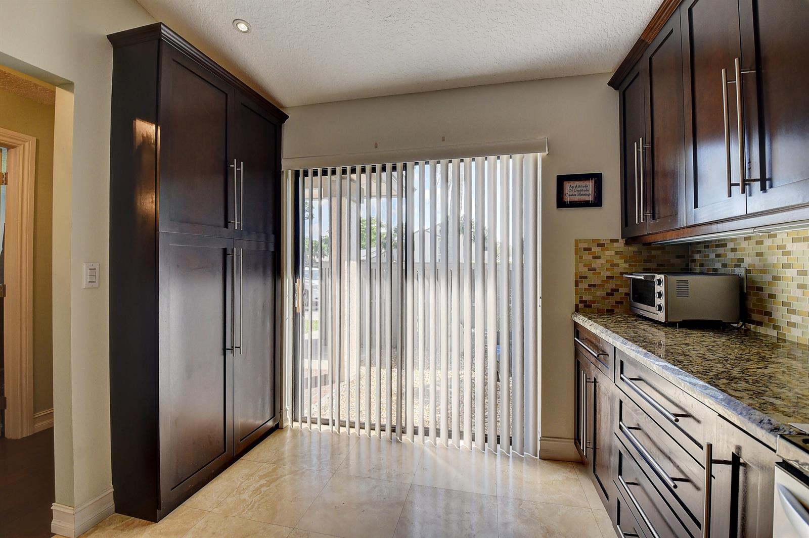 A kitchen featuring dark wood cabinetry, granite countertops, tile flooring, and a sliding glass door — 8458 Boca Glades Boulevard E, Boca Raton FL 33434, BOCA RATON, FL