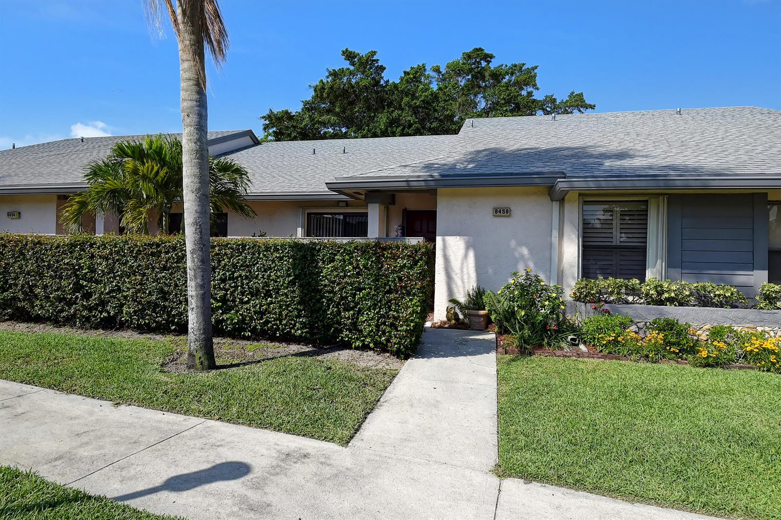 A single-story house with a gray roof, beige stucco walls, and a manicured hedge — 8458 Boca Glades Boulevard E, Boca Raton FL 33434, BOCA RATON, FL