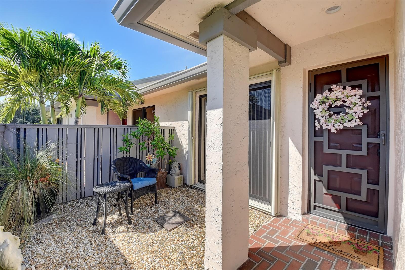 A front entryway features a brick patio, a gravel seating area, and a decorative door — 8458 Boca Glades Boulevard E, Boca Raton FL 33434, BOCA RATON, FL