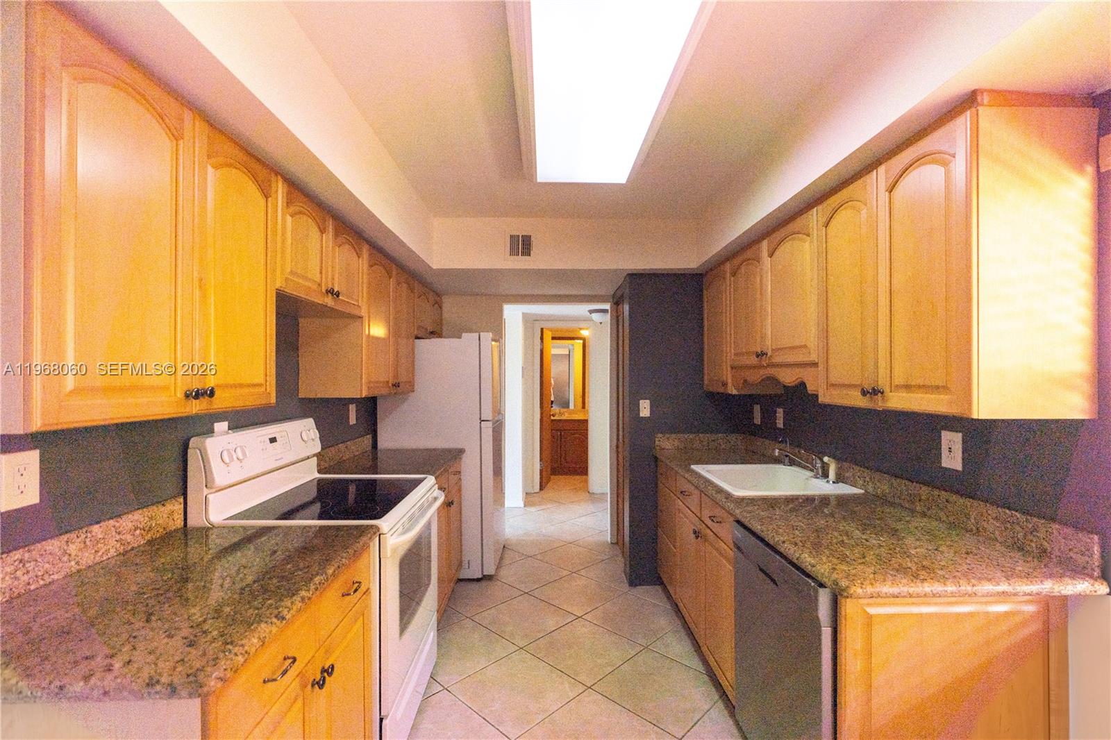 A galley kitchen features light wood cabinets, granite countertops, and a white stove — 430 Commodore Dr # 314, Plantation FL 33325, PLANTATION, FL
