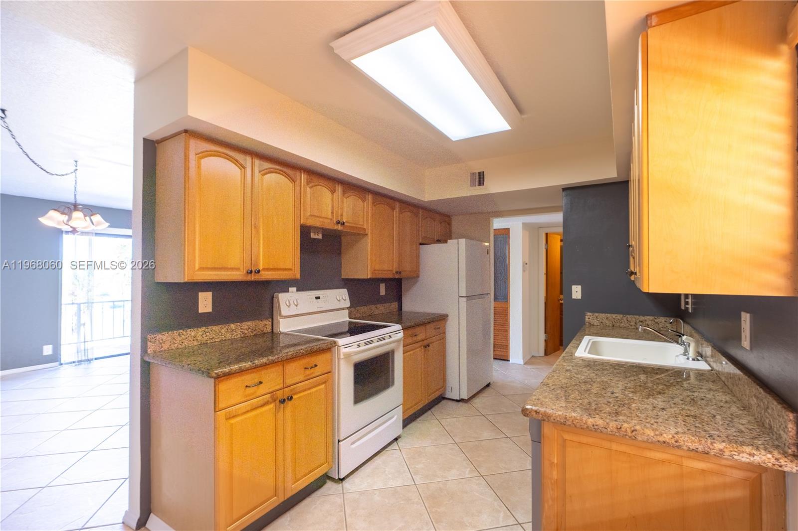 A kitchen features light wood cabinets, granite countertops, white appliances, and dark gray walls — 430 Commodore Dr # 314, Plantation FL 33325, PLANTATION, FL