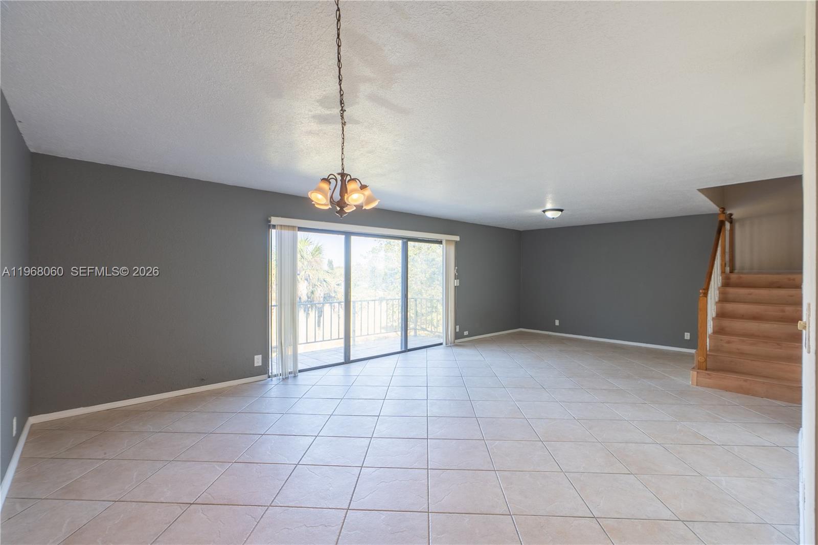 An empty room features gray walls, tiled flooring, a chandelier, and a wooden staircase — 430 Commodore Dr # 314, Plantation FL 33325, PLANTATION, FL