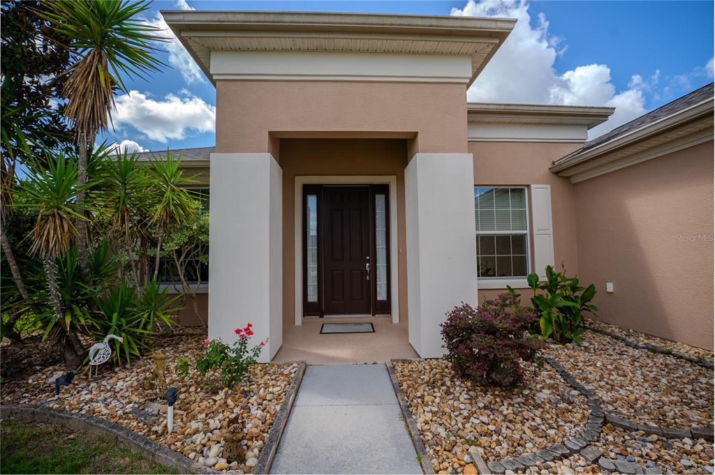 The front entrance of a tan stucco house features a dark door and rock landscaping — 9876 SW 69TH LANE, OCALA, FL