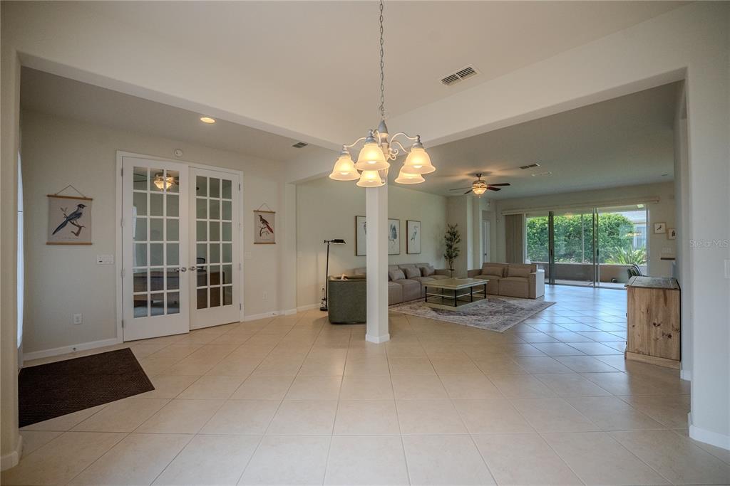 A spacious room with tile flooring, a central chandelier, and a living area beyond — 9876 SW 69TH LANE, OCALA, FL