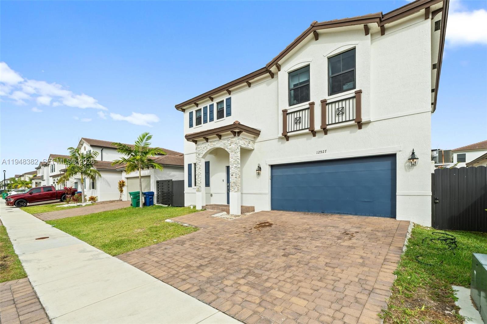 A two-story house features a blue garage door, stone accents, and a paved driveway — 12927 SW 229th Ter, Miami FL 33170, MIAMI, FL